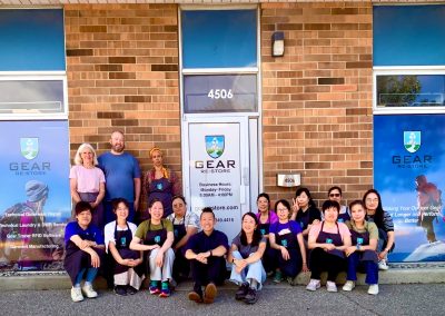Group of Gear re-Store team members posing in front of the brick storefront at 4506, Canada's Gear re-Store's location, wearing company aprons and smiling beneath the Gear Re-Store signs.